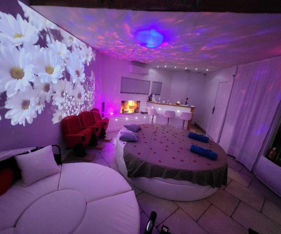 Habitación con iluminación púrpura, mesa y sillas en Chambre LOVE ROOM 35m2 avec LIT ROND Balnéo Hammam vidéoprojecteur, en Jardin
