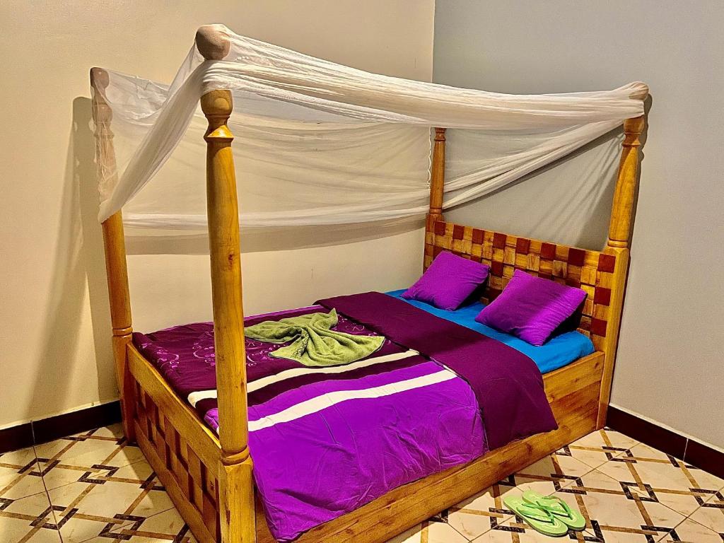 1 dormitorio con cama de madera con sábanas moradas en Roots cottages and campsite, 