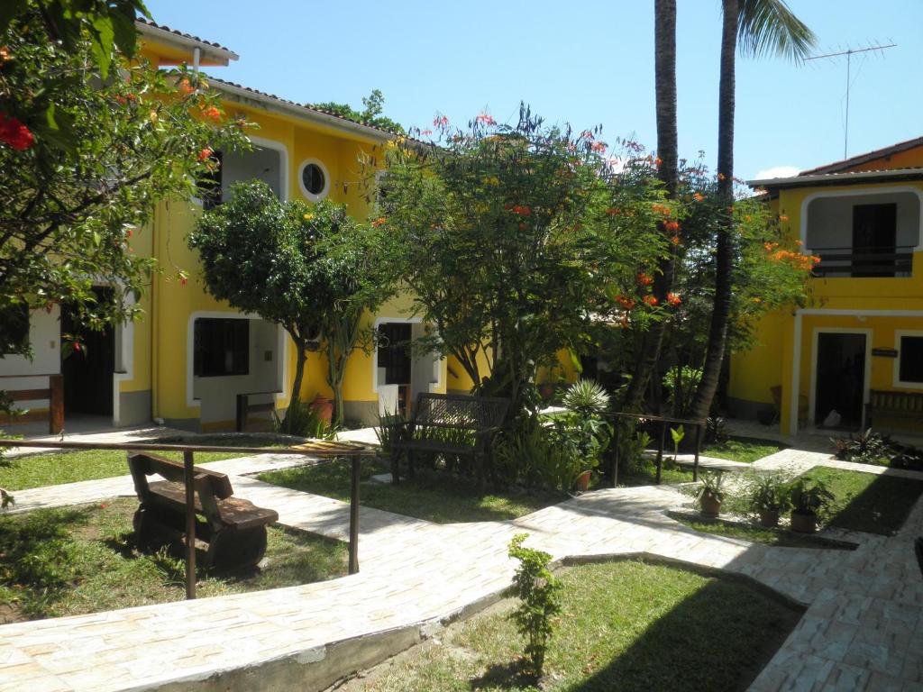 a yellow house with trees and benches in a yard at Aguamarinha Pousada in Porto De Galinhas