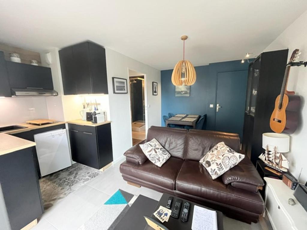 - un salon avec un canapé en cuir brun et une guitare dans l'établissement Bel appartement 3 pièces avec WIFI, proche plage et commerces, balcon et parking privé. - FR-1-712-79, à Villers-sur-Mer