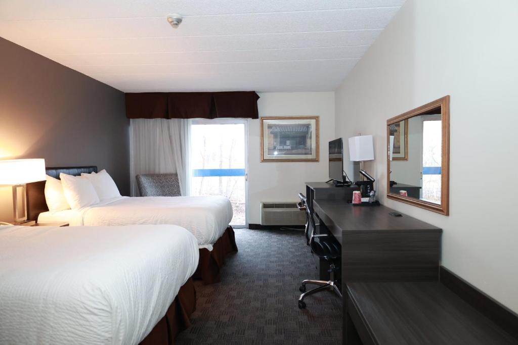 a hotel room with two beds and a desk with a mirror at Days Inn by Wyndham Sudbury & Conference Centre in Sudbury