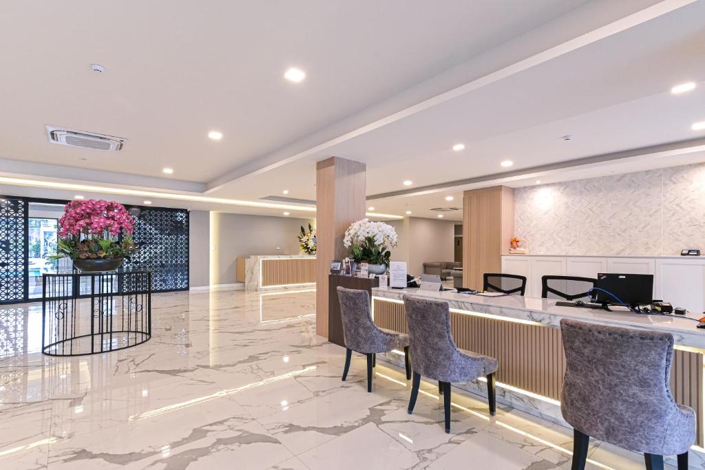 A polished lobby reception area combines a long desk, upholstered guest chairs, marble-patterned floors and flower arrangements.