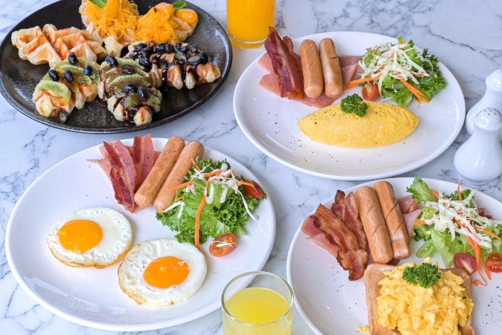 A close-up breakfast spread combines eggs, sausages, bacon, salad, juice and assorted fruit pastries.