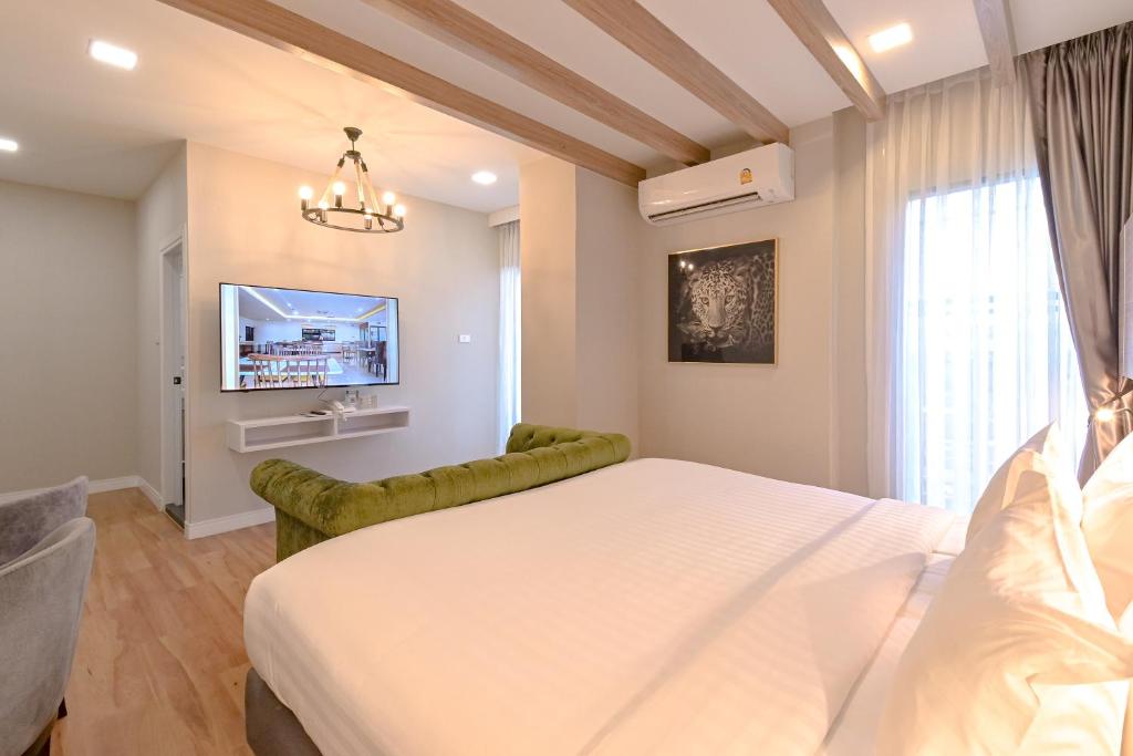 A bedroom-living area with a large bed, green sofa, wall-mounted TV and bright curtained window.