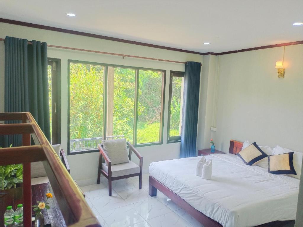 een slaapkamer met een bed, een stoel en ramen bij Dokchampa Hotel in Vang Vieng