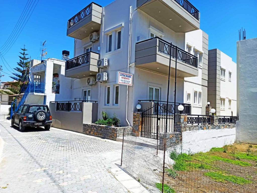 um edifício branco com varandas e um carro estacionado em frente em Litsa Mare Apartments em Agia Pelagia