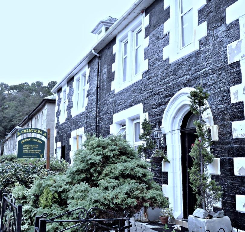 een zwart bakstenen gebouw met een boom ervoor bij Arbour Guest House in Oban