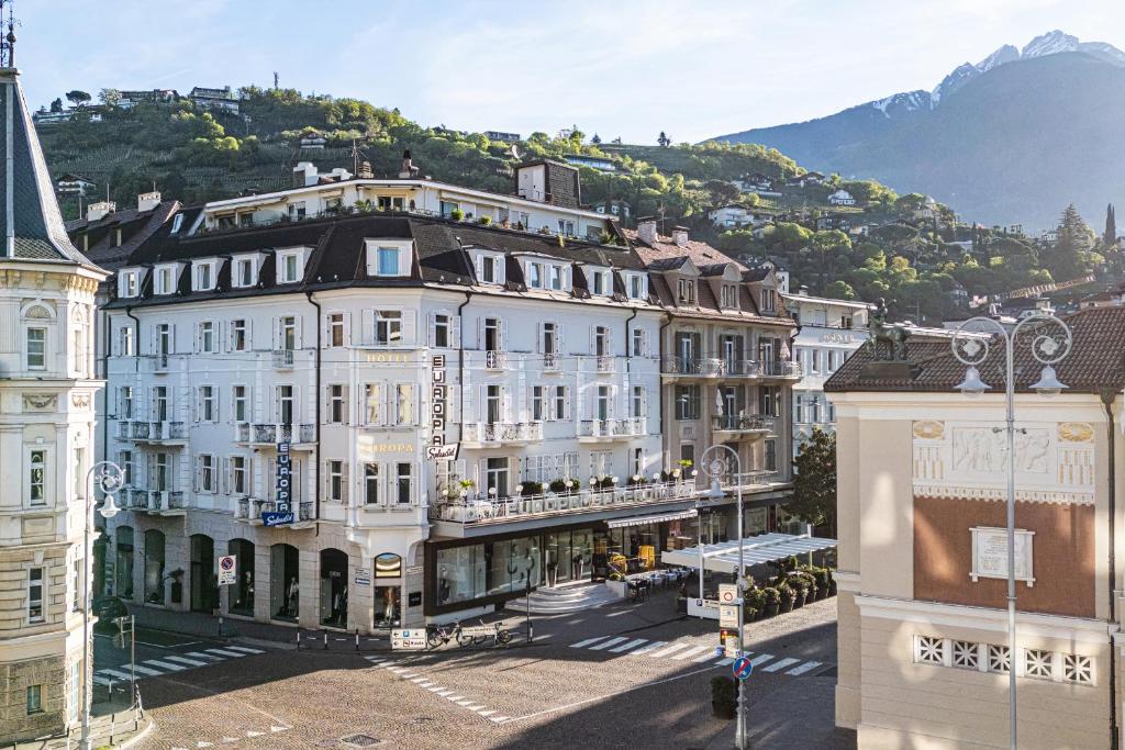 un grand bâtiment blanc avec une montagne en arrière-plan dans l'établissement Hotel Europa Splendid, à Merano