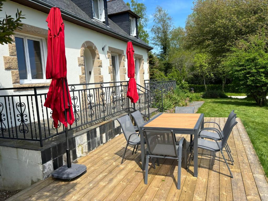 una terraza de madera con mesa y sillas con sombrillas rojas en Maison Plélauff, en Plélauff