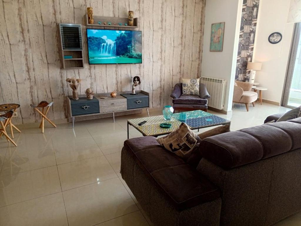 uma sala de estar com um sofá e uma televisão na parede em Chaletapartment in Tilal Fanar resort, em Mār Yūsuf