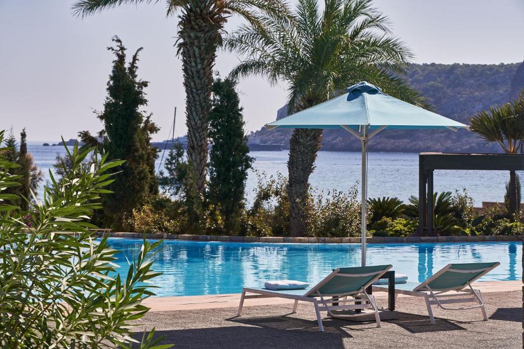 two chairs and an umbrella next to a swimming pool at Aquagrand Exclusive Deluxe Resort Lindos - Adults only in Lindos