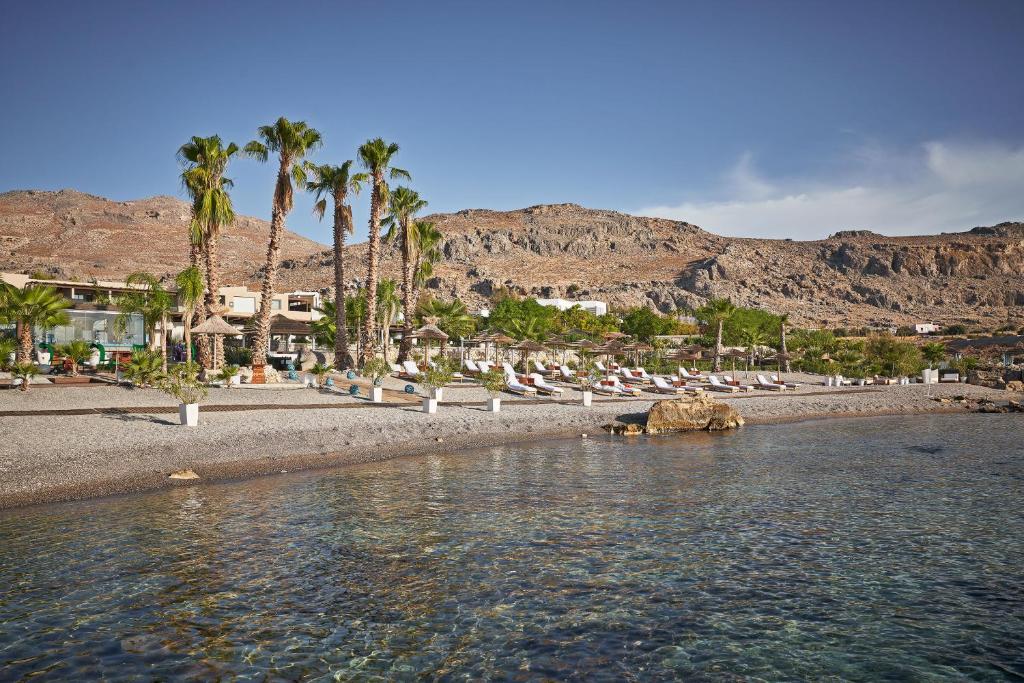 a beach with palm trees and buildings and water at Aquagrand Exclusive Deluxe Resort Lindos - Adults only in Lindos