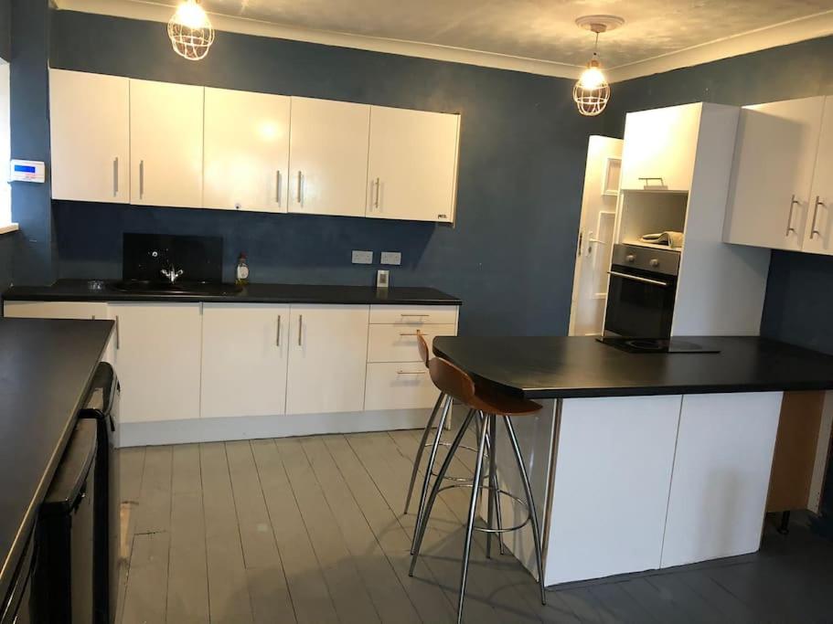 eine Küche mit weißen Schränken und einer schwarzen Arbeitsplatte in der Unterkunft 9 bed house with garden & parking in Iford
