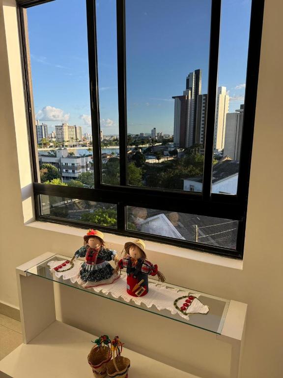 two dolls sitting on a shelf in front of a window at Flat na melhor localização in Campina Grande