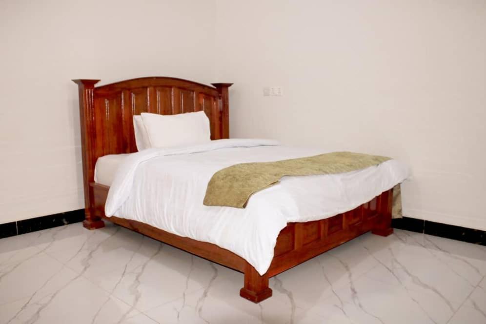 a bedroom with a wooden bed with white sheets at Latitude Lukozi Hotel in Hambayo
