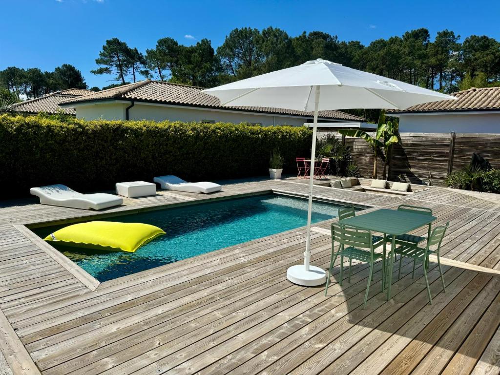 een zwembad met een parasol, een tafel en een stoel bij Maison vacances Bassin d'Arcachon in Gujan-Mestras