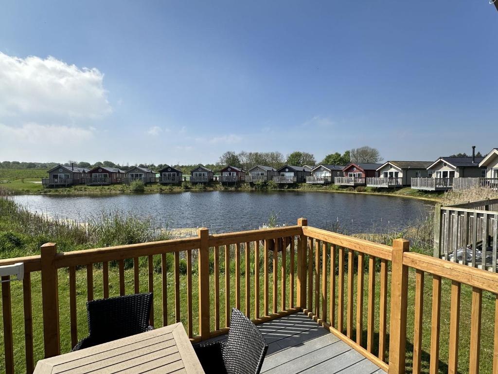 una terraza de madera con sillas y un lago con casas en Low Lake Lodge en Reighton