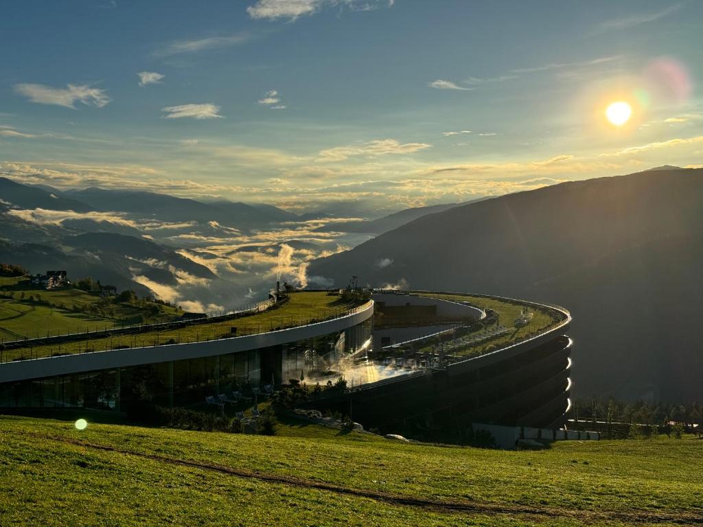 un bâtiment sur une colline avec le soleil en arrière-plan dans l'établissement Familienhotel Familiamus, à Maranza