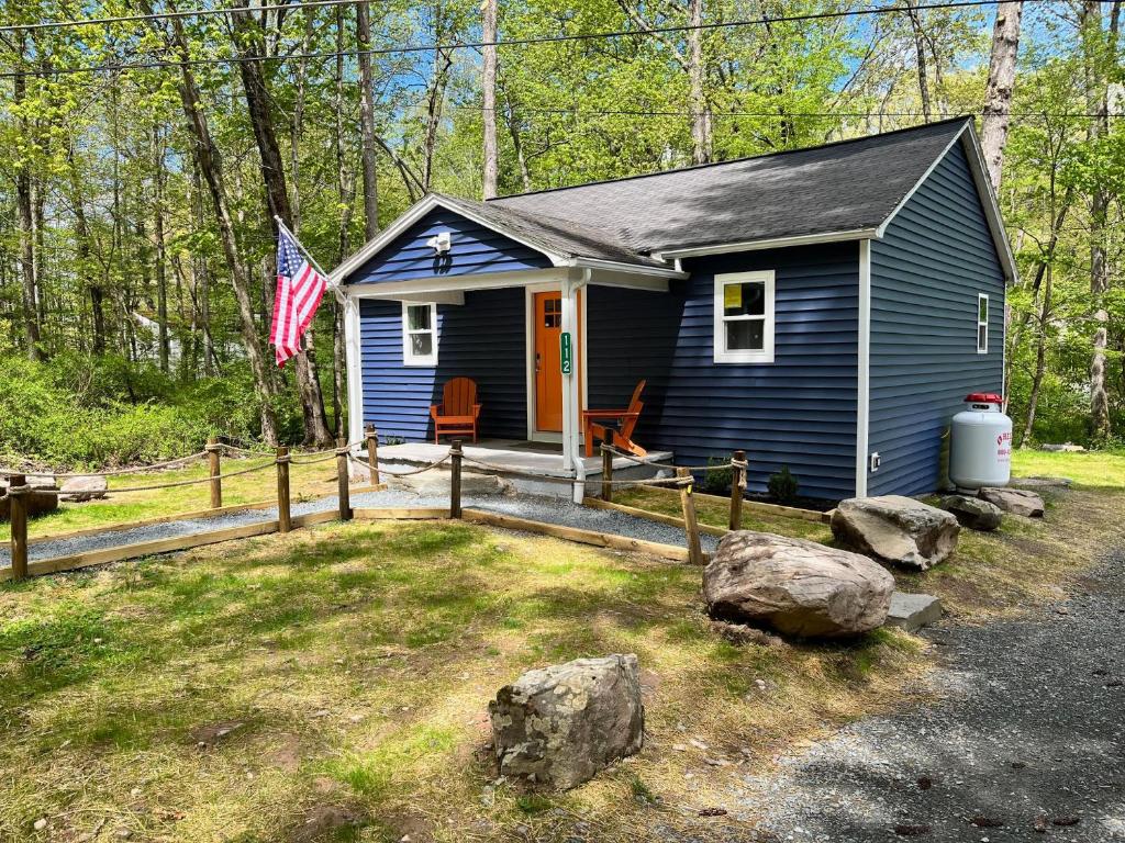 ein kleines blaues Haus im Wald mit amerikanischer Flagge in der Unterkunft Bear Run Bungalow in Hawley