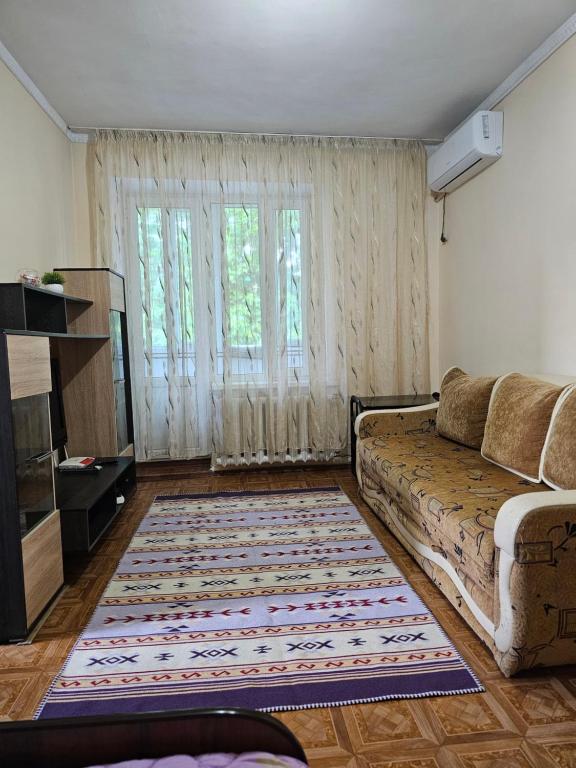 een woonkamer met een bank en een groot raam bij Apartment Seifullina473 in Alma-Ata