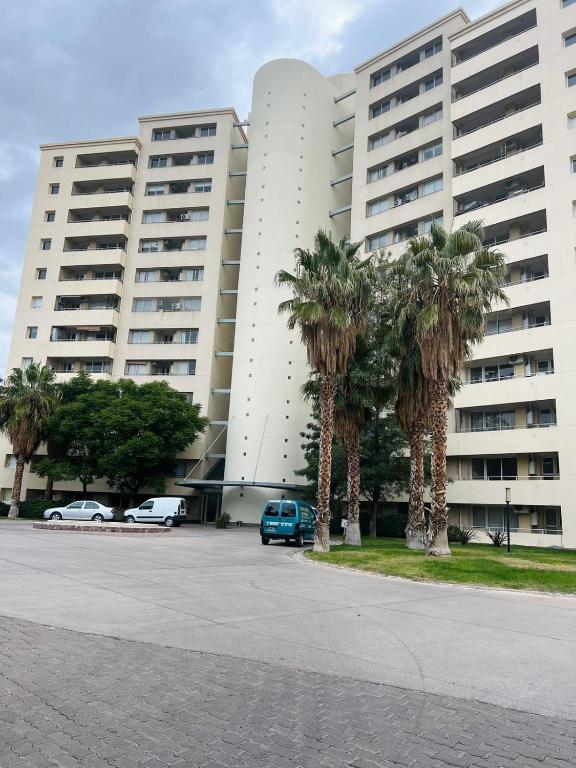 um parque de estacionamento em frente a um grande edifício com palmeiras em Depto. a estrenar en Mendoza. em Las Heras