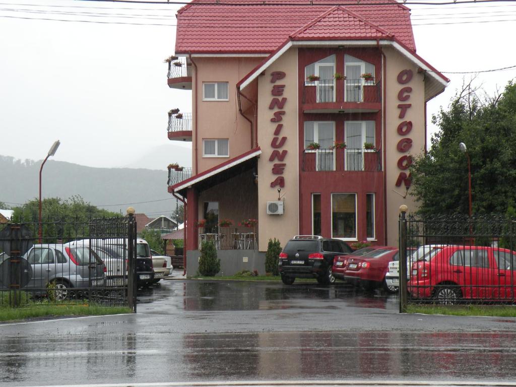 a building in the rain with cars parked in a parking lot at Pensiunea Octogon in Piatra Neamţ