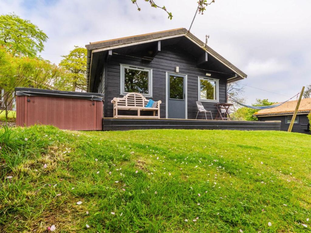 a black tiny house with a bench on a lawn at Chalet Oak Hot Tub Lodge by Interhome in Launceston