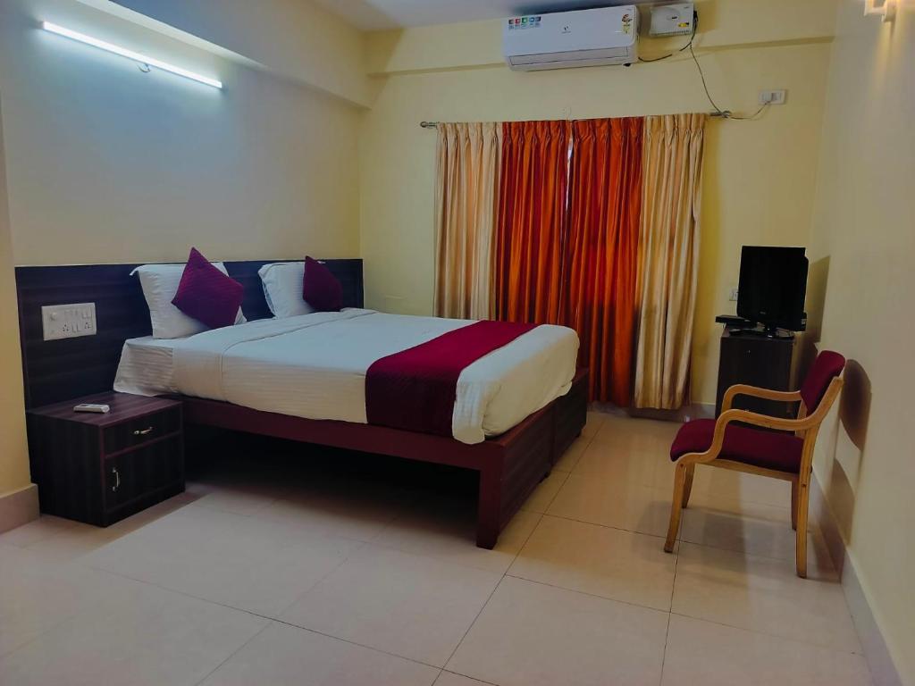 a hotel room with a bed and a chair at Hotel Vyshak International in Mysore