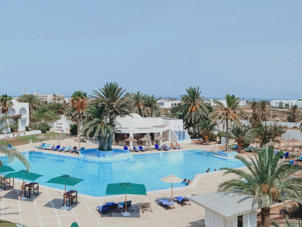 an overhead view of a large swimming pool with palm trees at Hotel Bougainvillier Djerba in Taguermess