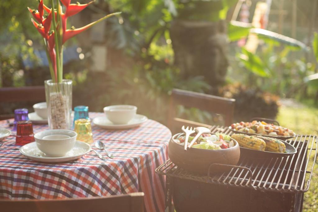 An outdoor breakfast table with coffee, fruit and grilled food in a leafy garden.