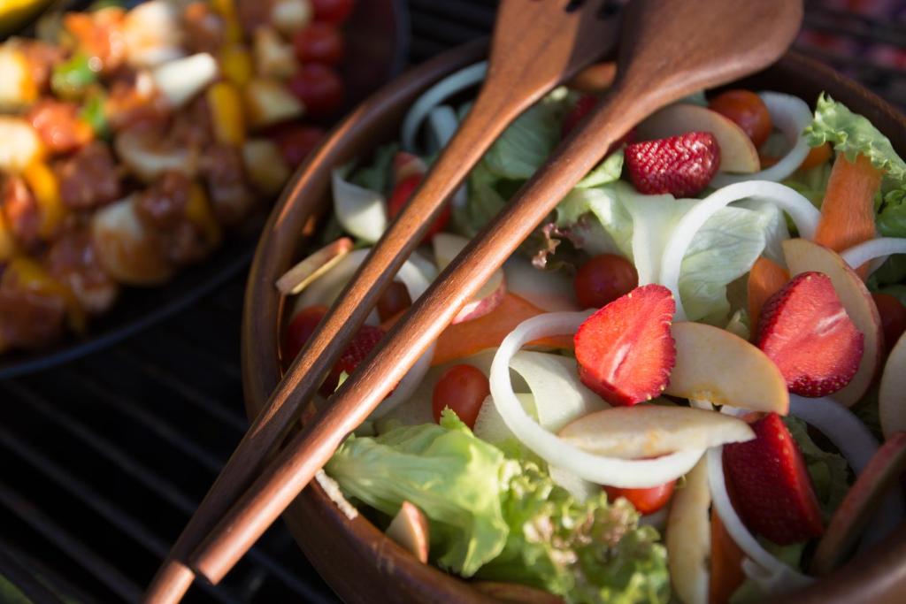 A fresh salad with fruit and vegetables is served with wooden utensils.