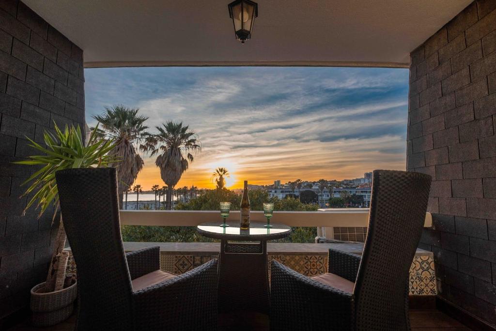 Sea View W Balcony 2 Mins Walk To Beach & Casino في استوريل: شرفة مع طاولة وكراسي وإطلالة على غروب الشمس