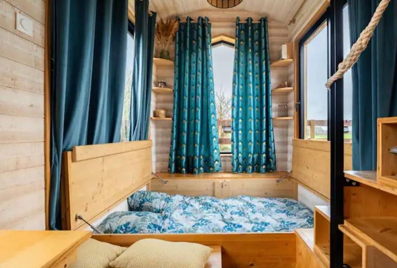 Habitación pequeña con cortinas azules y cama en La Tiny Breizh, en La Poëtevinière