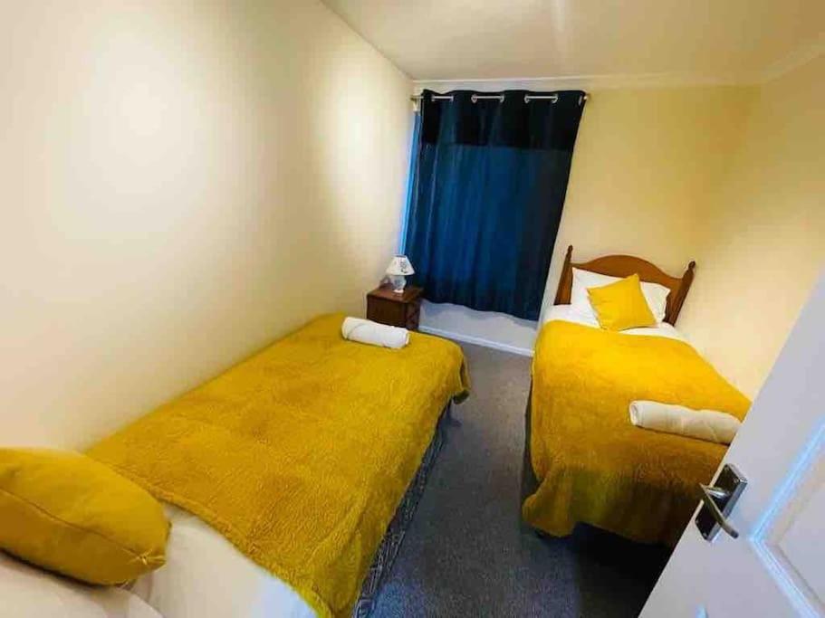 duas camas num quarto com lençóis amarelos em Cosy 1st floor 2 bedroom flat em Little Paxton