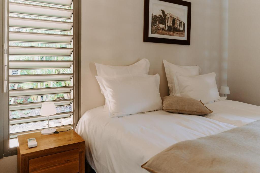 Habitation TABANON في بيتي-بور: سرير بملاءات ومخدات بيضاء بجانب نافذة
