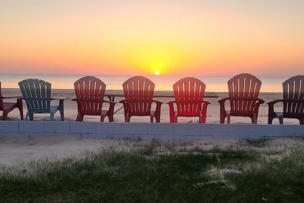 a group of chairs sitting on the beach at sunset at Lake Huron - 3 Bedroom, 2 Bath Lake Front Home (Sleeps 12) in Oscoda