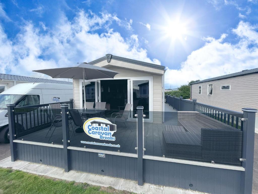 une grande terrasse avec un parasol et une camionnette dans l'établissement Golden Palm Resort - The Cambridge Deluxe - Coastal Caravan Breaks, à Chapel St. Leonards