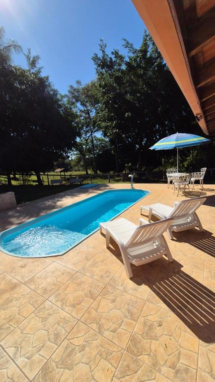 a pair of chairs and an umbrella next to a swimming pool at Sítio Canto da Seriema in Torrinha