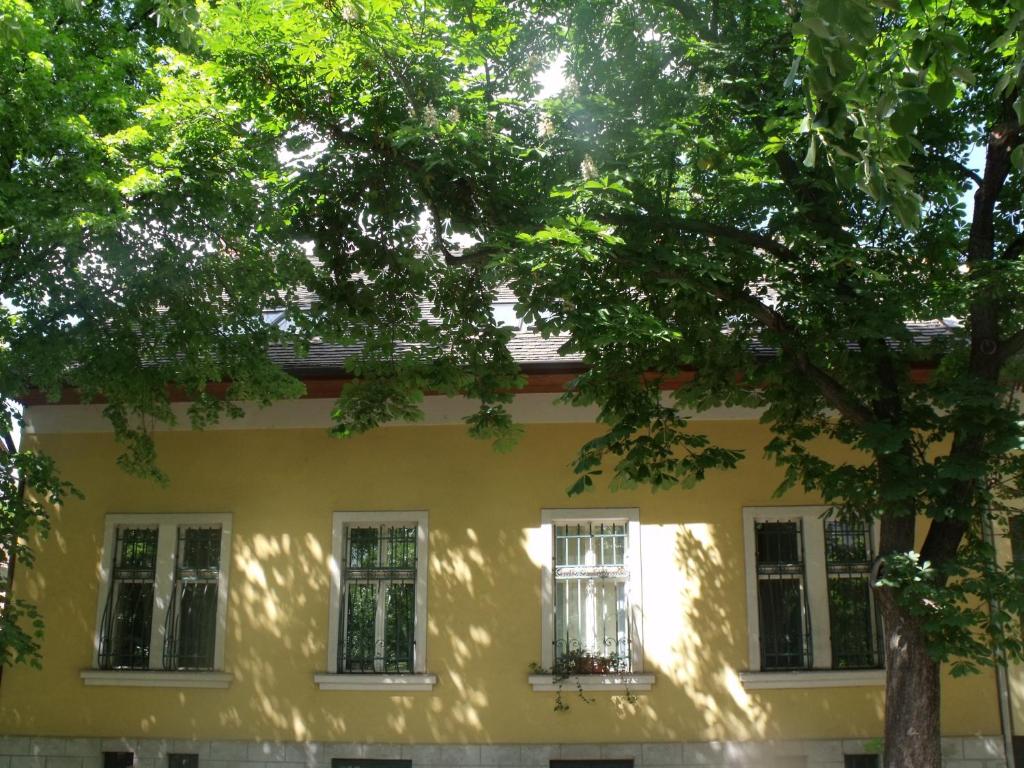 a yellow house with white windows and a tree at Adalbert Ház in Budapest