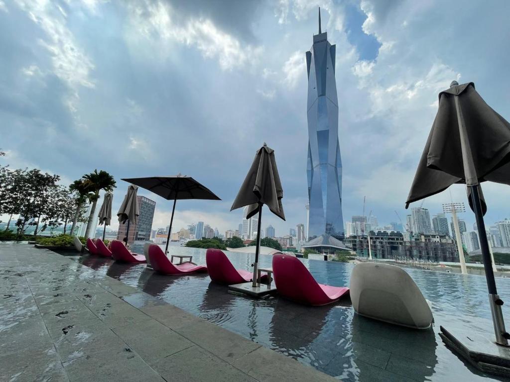 a row of chairs and umbrellas in a pool with the burj at Opus Residence Kuala Lumpur By Great Service in Kuala Lumpur