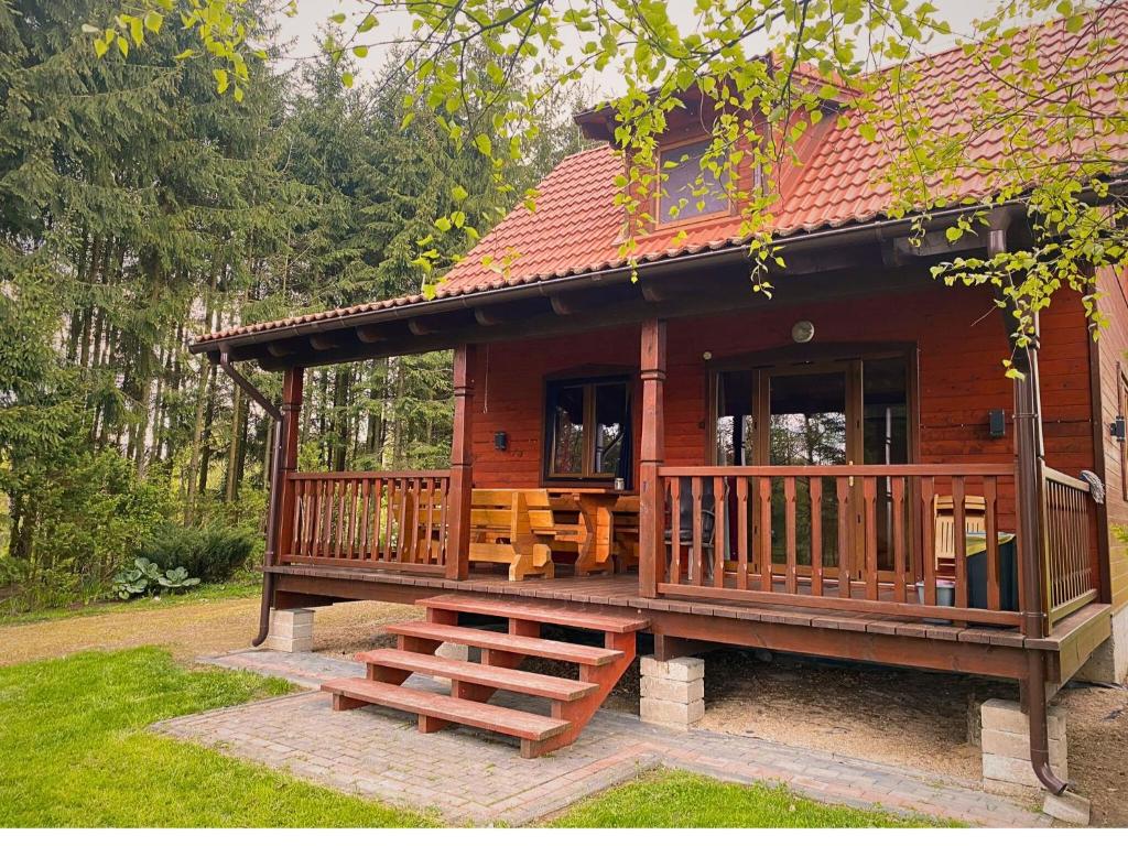 a small wooden cabin with a porch and a bench at Domek Pod Lasem in Pozezdrze