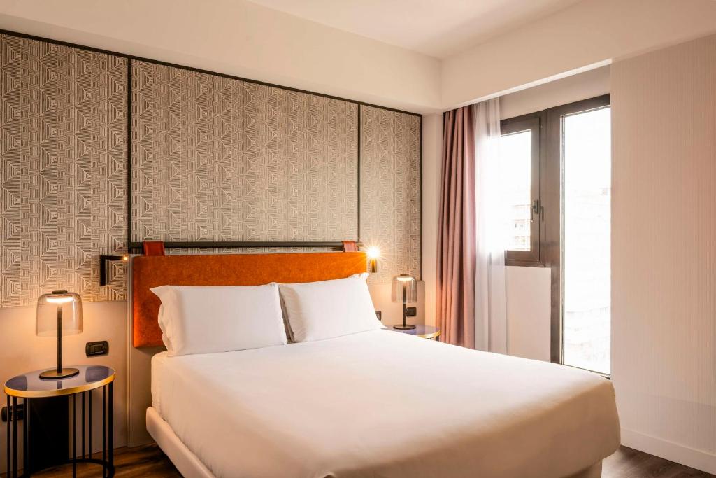 a bedroom with a large white bed and a window at NH Catania Centro in Catania