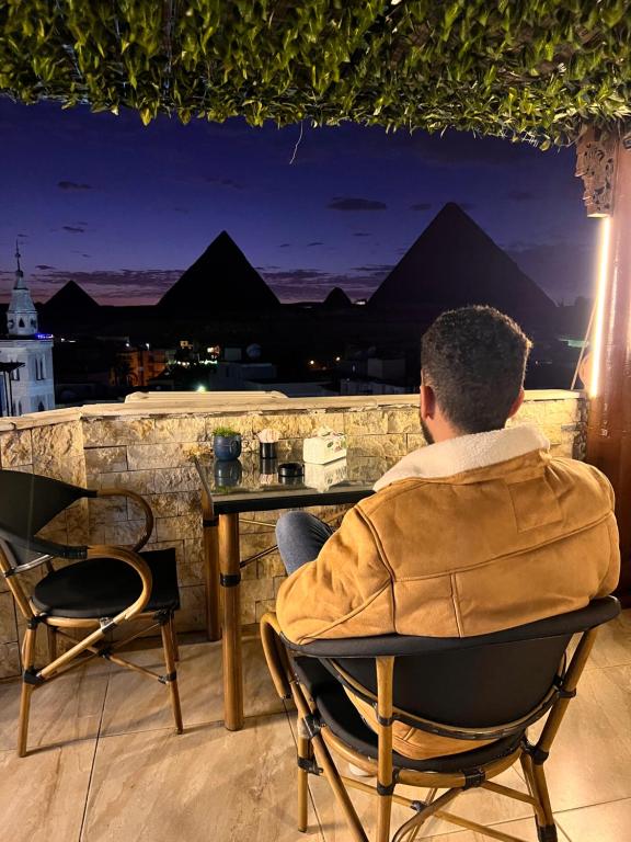un hombre sentado en una mesa en un balcón por la noche en Imhotep pyramids INN en El Cairo