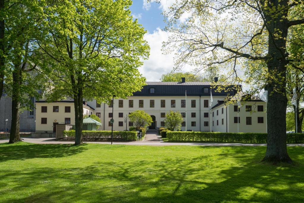 un grand bâtiment blanc avec des arbres au premier plan dans l'établissement Vadstena Klosterhotell Konferens & Spa, à Vadstena