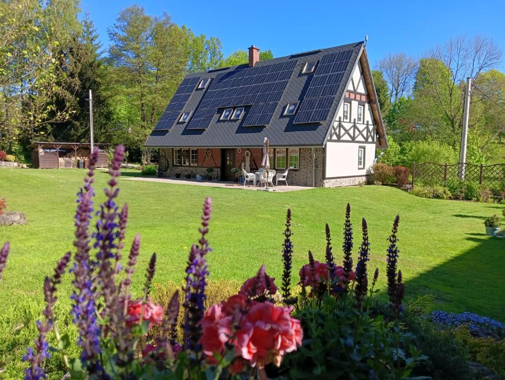 a house with a solar roof with flowers in the foreground at Agroturystka Taszówka in Taszów