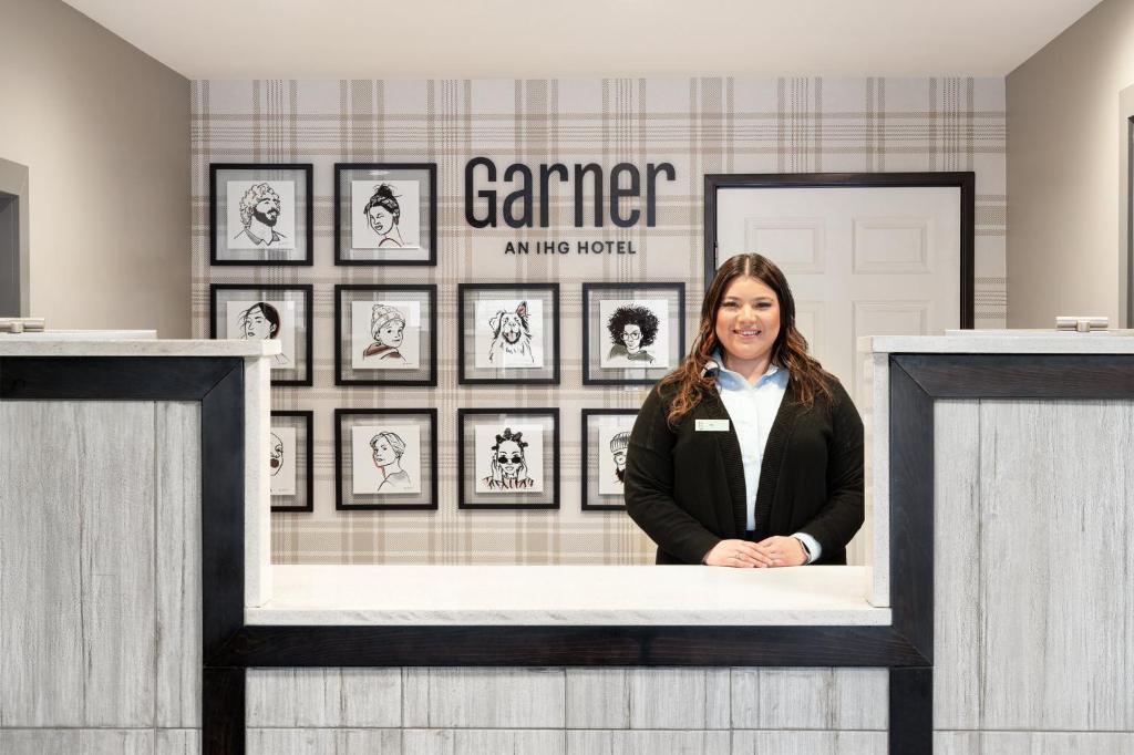 una mujer de pie detrás de un mostrador en una habitación con cuadros enmarcados en Garner Hotel Auburn - Seattle, an IHG Hotel en Auburn