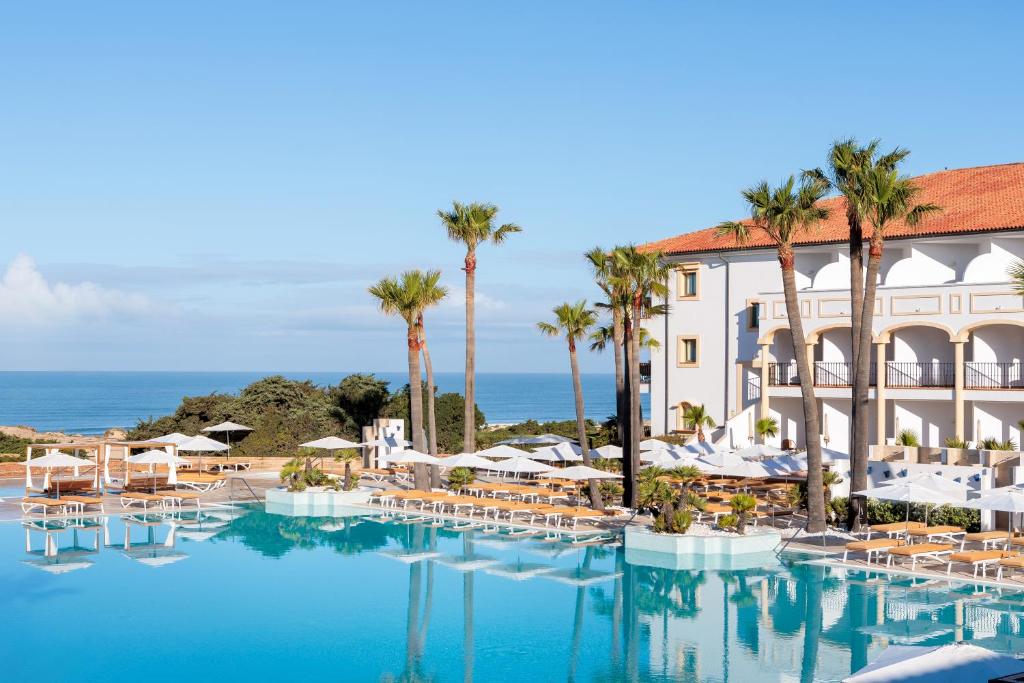 un hôtel avec une piscine bordée de chaises et de palmiers dans l'établissement Iberostar Selection Andalucia Playa, à Chiclana de la Frontera