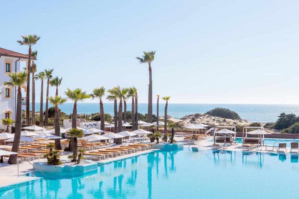 a swimming pool with chairs and palm trees and the ocean at Iberostar Selection Andalucia Playa in Chiclana de la Frontera