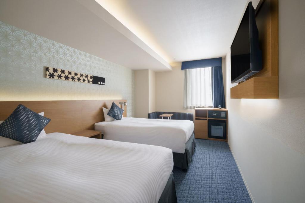 a hotel room with two beds and a flat screen tv at Hotel Vista Nagoya Nishiki in Nagoya