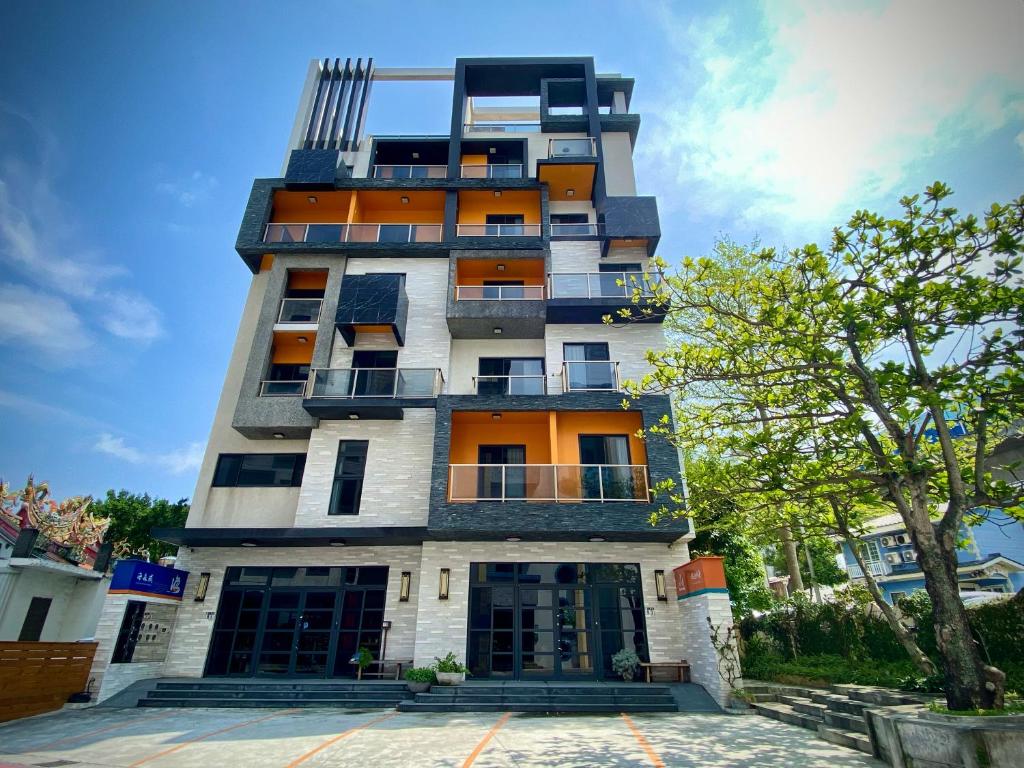 wysoki biały budynek z pomarańczowymi oknami i drzewem w obiekcie Hai Sheng Wei B&B w mieście Dahan